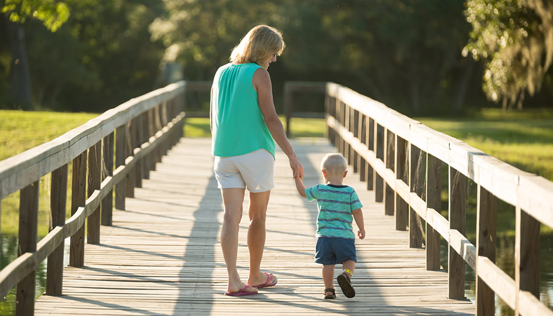 Mother and son holding hands and walking along a wooden bridge.