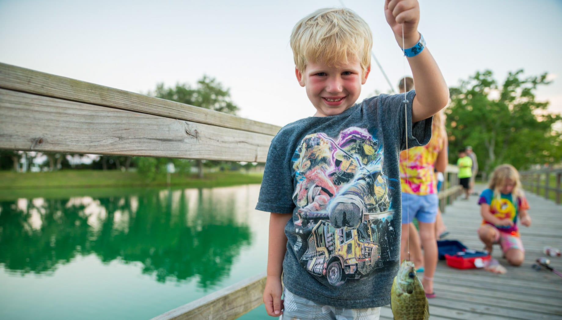 Boy on a wooden bridge holding a fish he just caught.