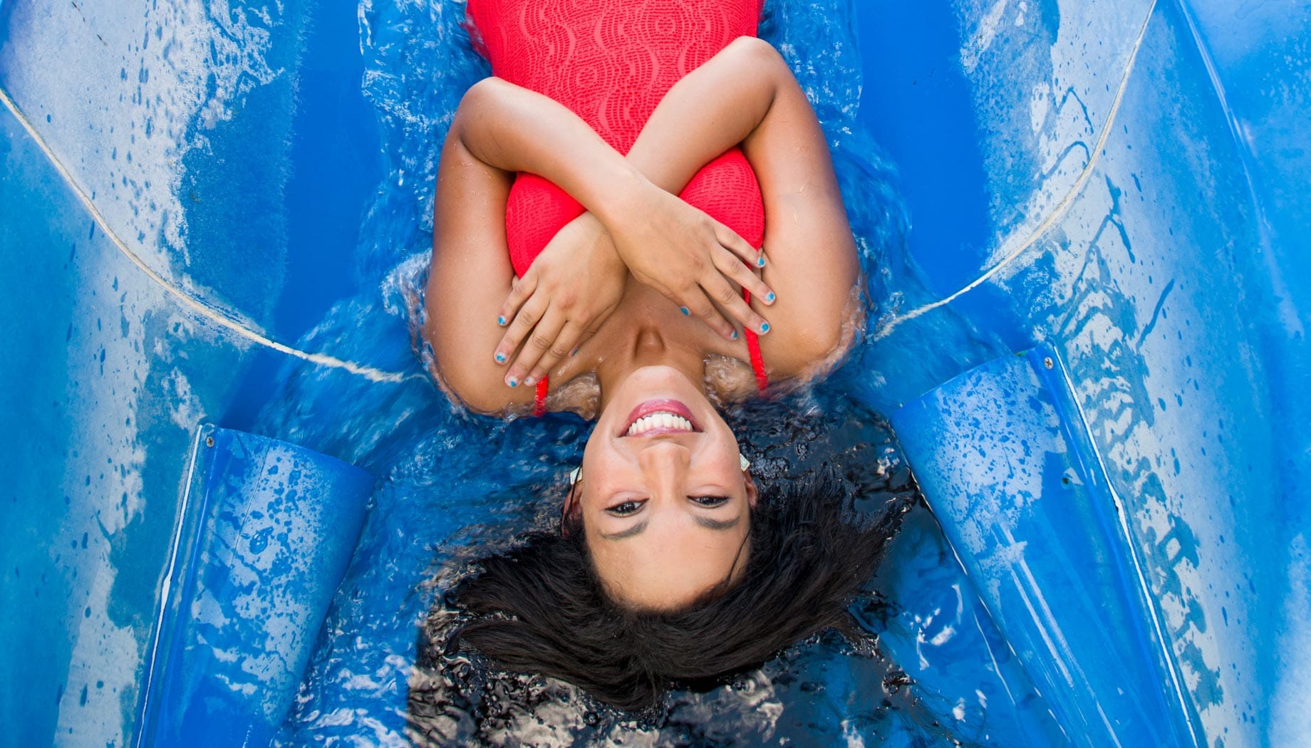 Woman in a red bathing suit with her hands across her chest and ready to go down a water slide.