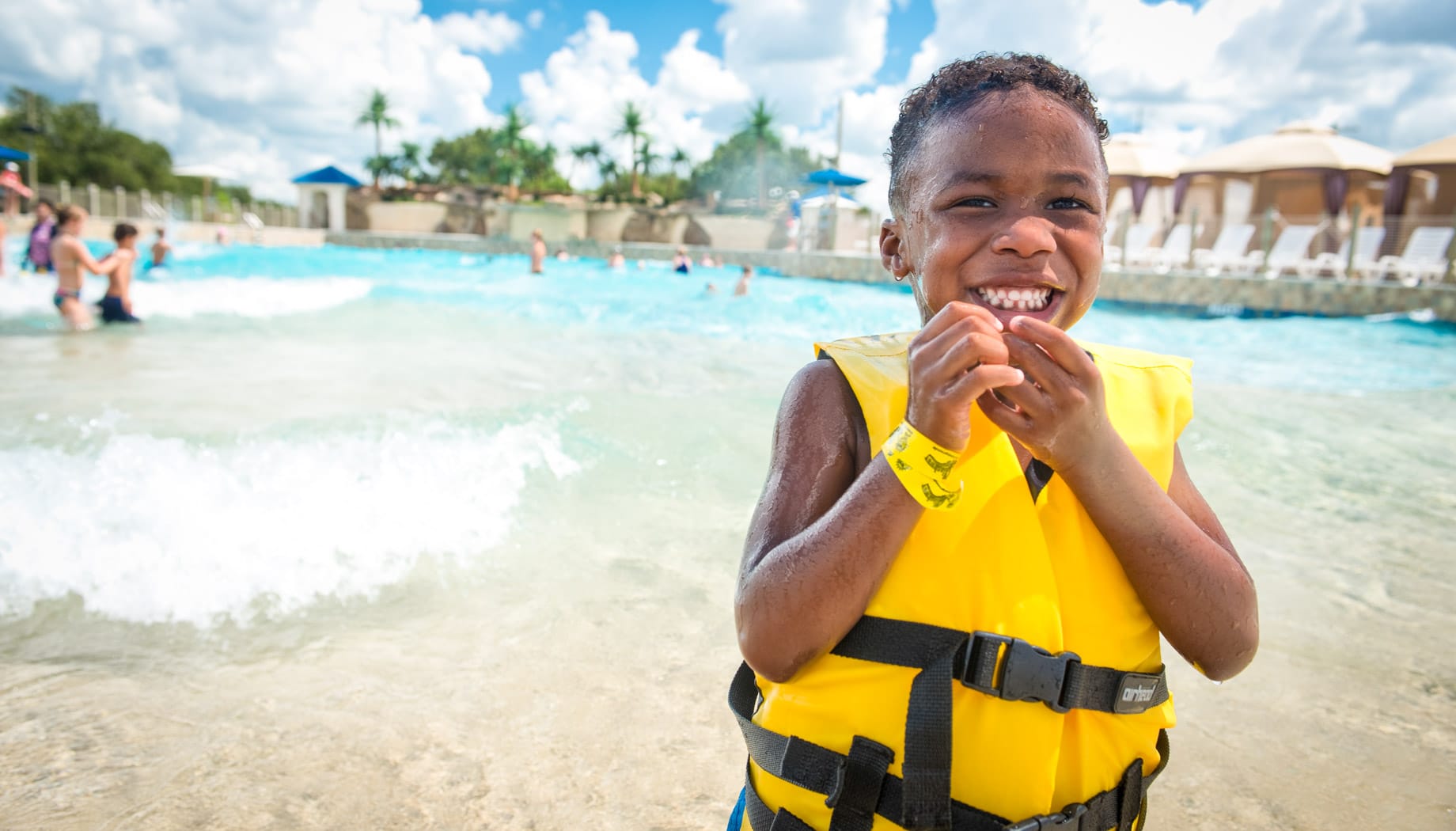 Boy in a yellow life jacket smiling and enjoying Splashway's Wavepool.