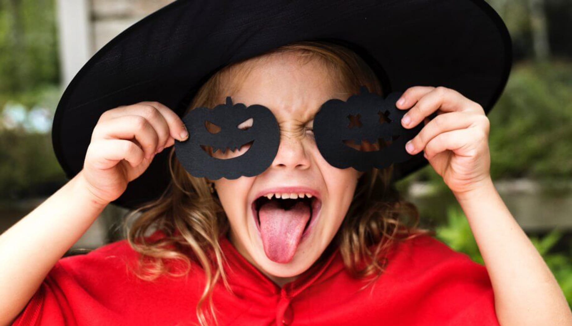 Girl in a witch hat holding black Halloween pumpkin cutouts.