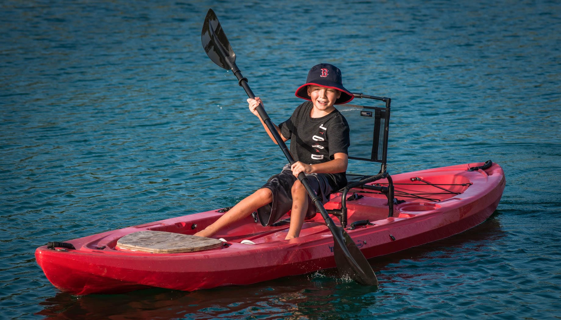 Boy kayaking in a red kayak on a pond.