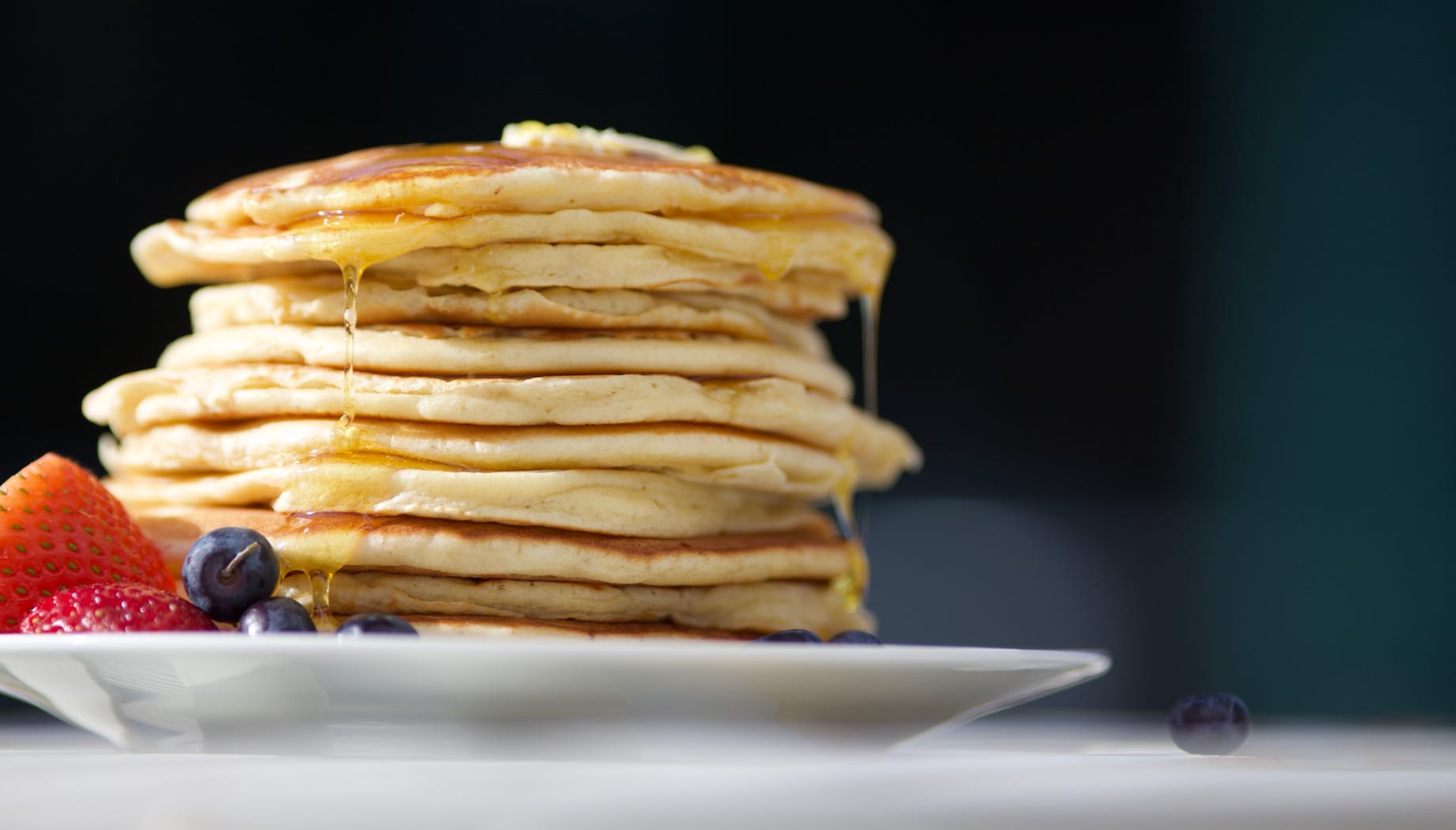 Stack of fluffy pancakes with butter on top and served with strawberries and blueberries.