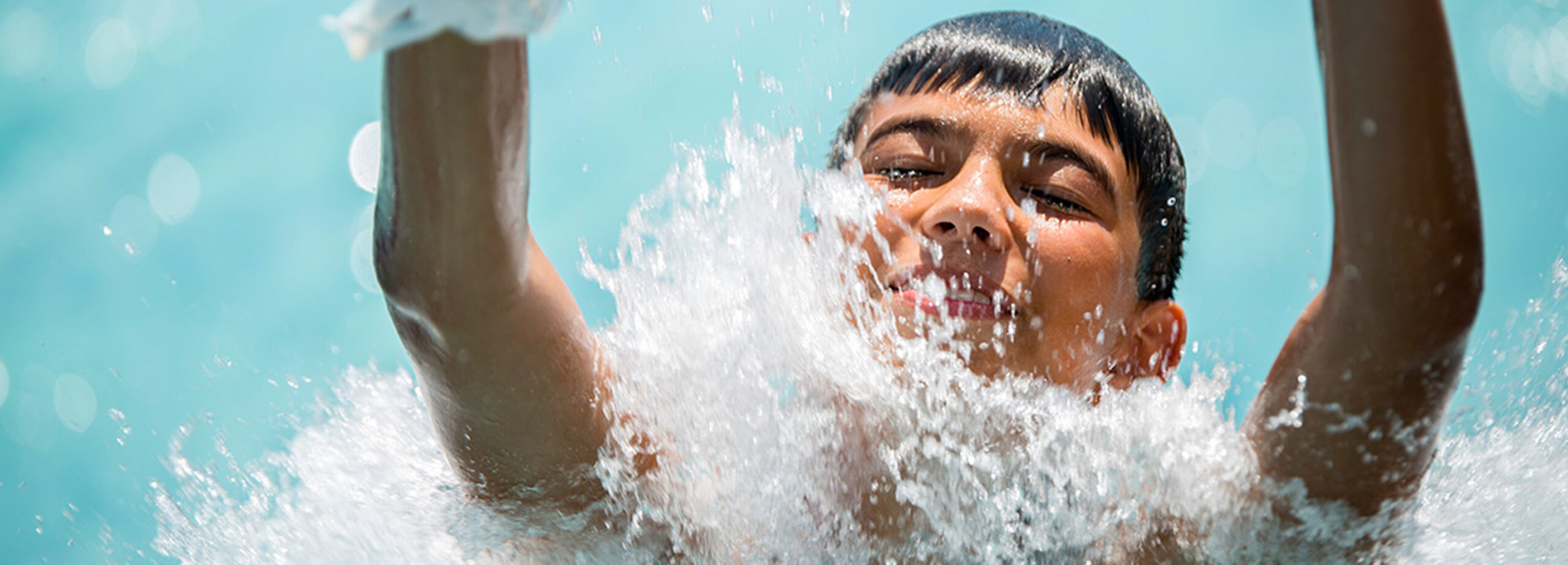 A person splashes into the water at the bottom of a water slide, with water droplets in the air and their feet visible in the foreground.