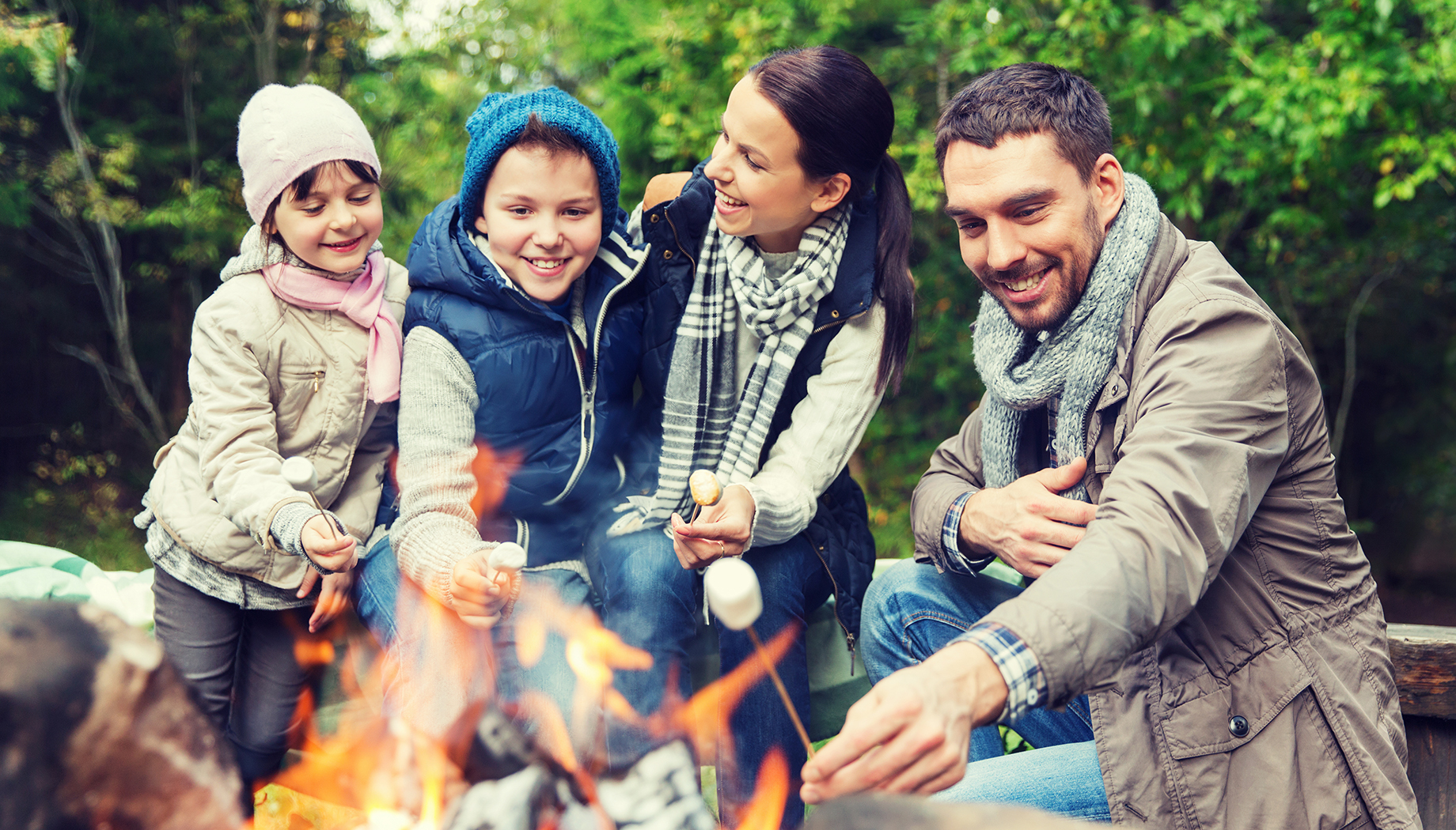 Family toasting marshmallows around a campfire in the woods.