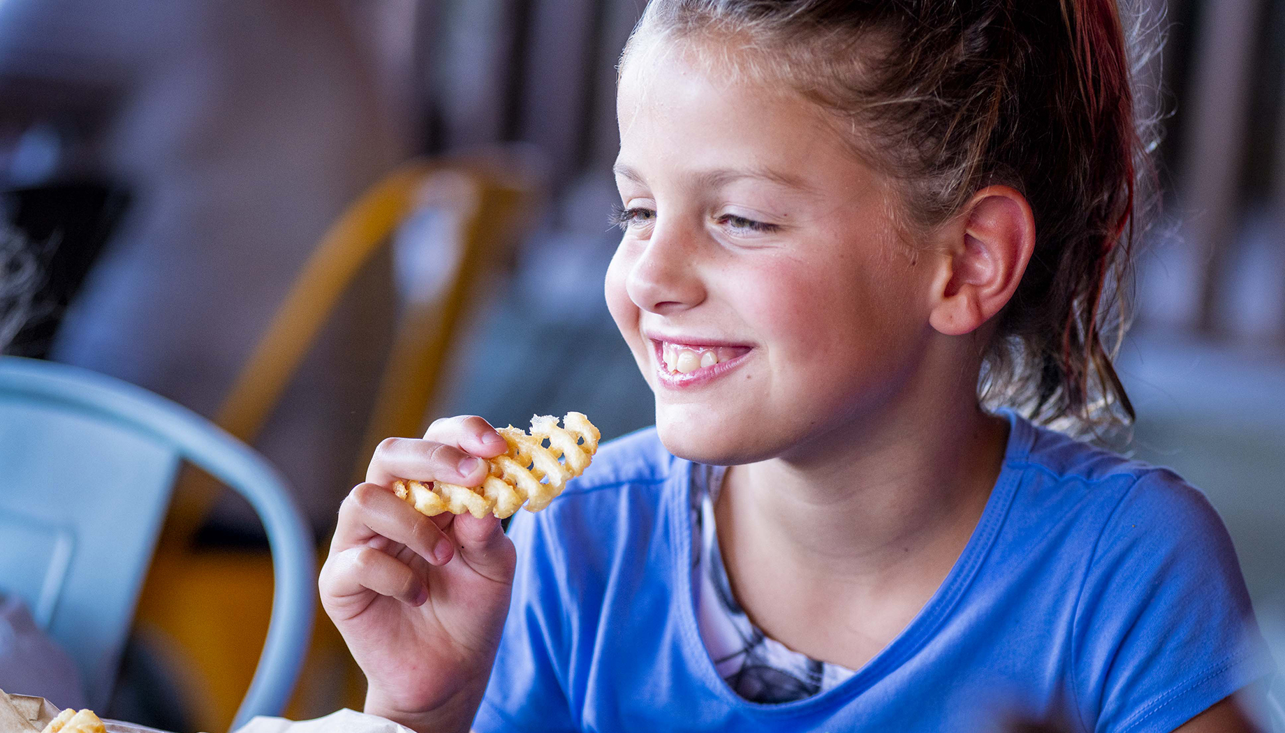 Girl in a blue shirt eating waffle fries.
