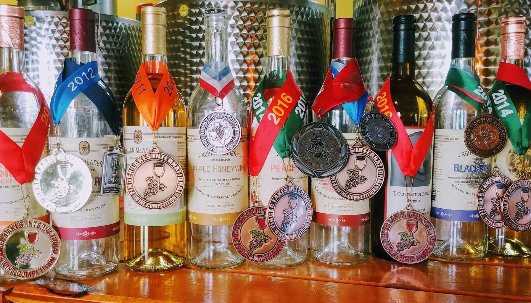 A row of wine bottles, each adorned with medals from various years, ranging from 2012 to 2016, and 2014.