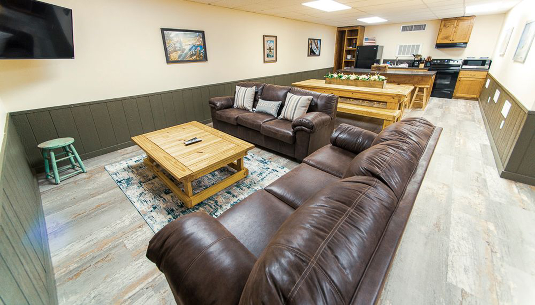 Living room with two brown leather couches, a wooden coffee table, a rug, wall decor, and an open kitchen area in the background.