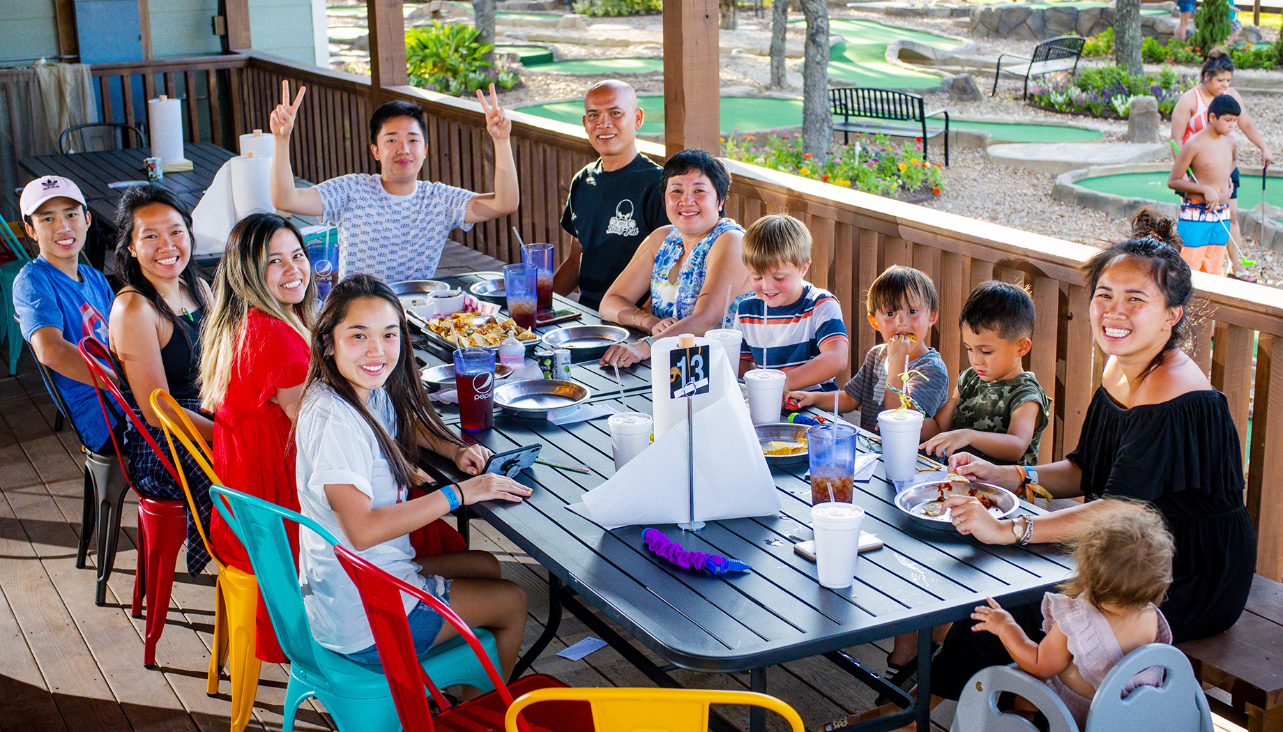 A group of people of various ages sitting around a large table outdoors, sharing a meal.