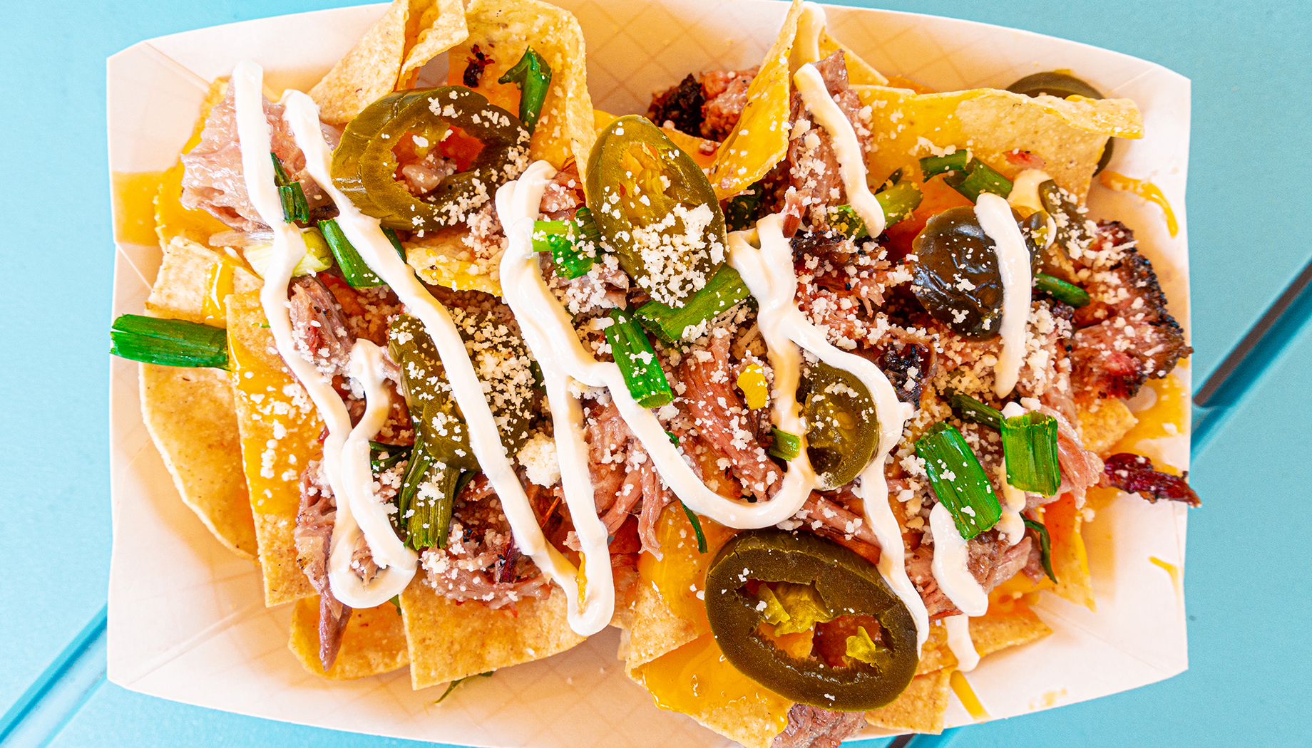 Nachos in a paper tray topped with barbecue meat, jalapeños, cheese, and more.