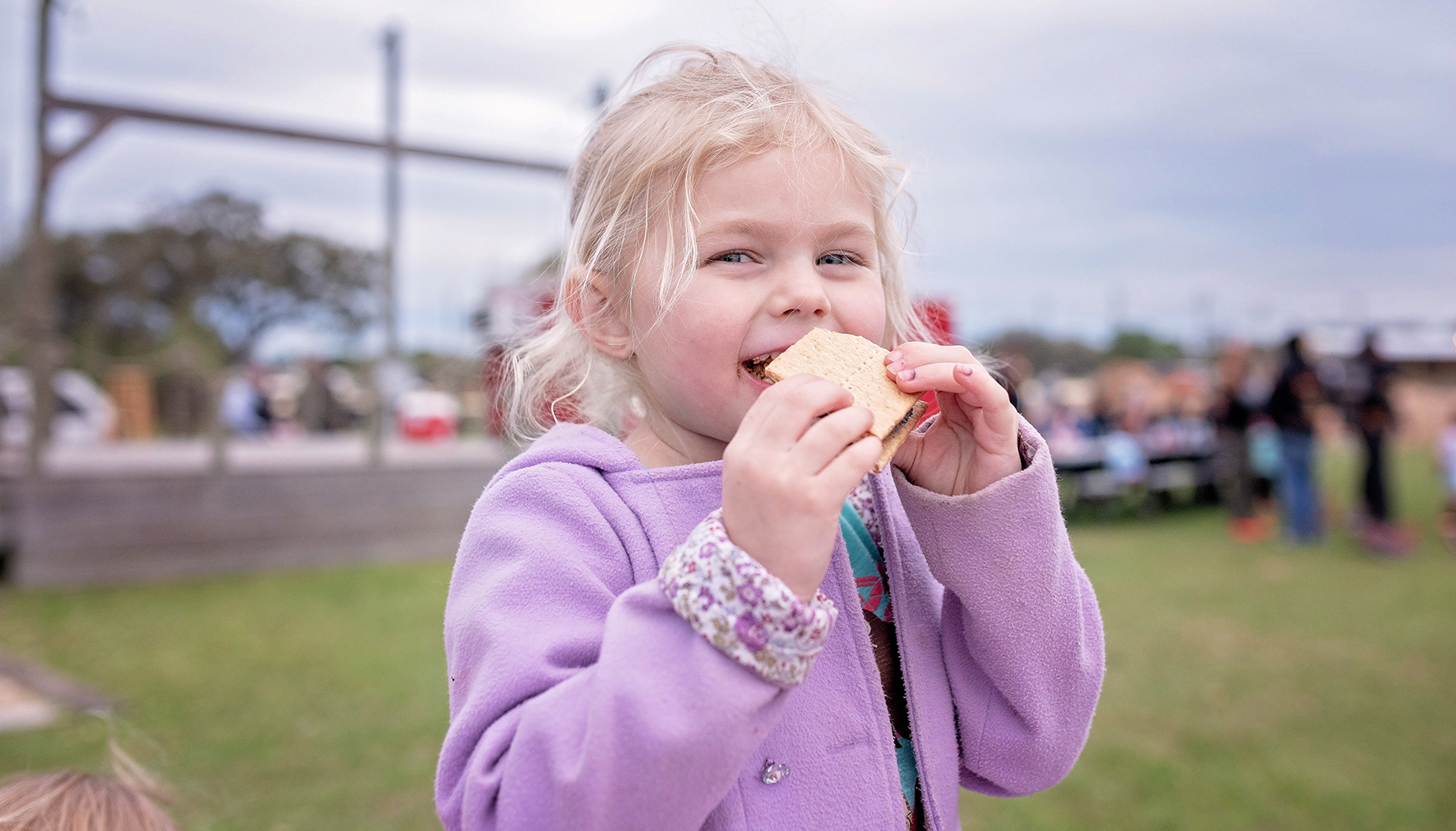 Girl in a purple jacket eating a smores.